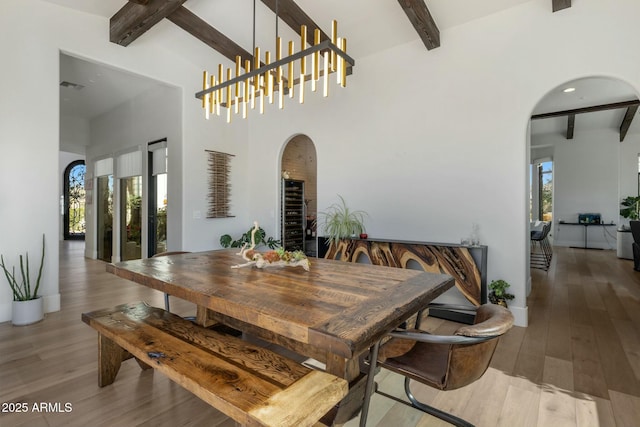 dining area featuring arched walkways, visible vents, beamed ceiling, and wood finished floors