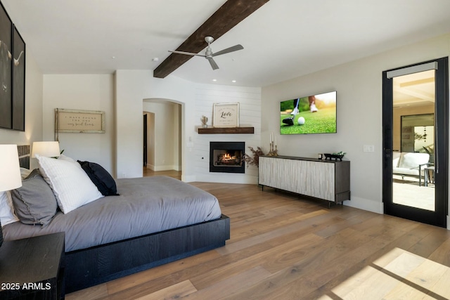 bedroom featuring arched walkways, wood finished floors, a large fireplace, and beam ceiling