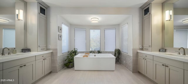 bathroom featuring a freestanding bath, two vanities, a sink, and tile walls