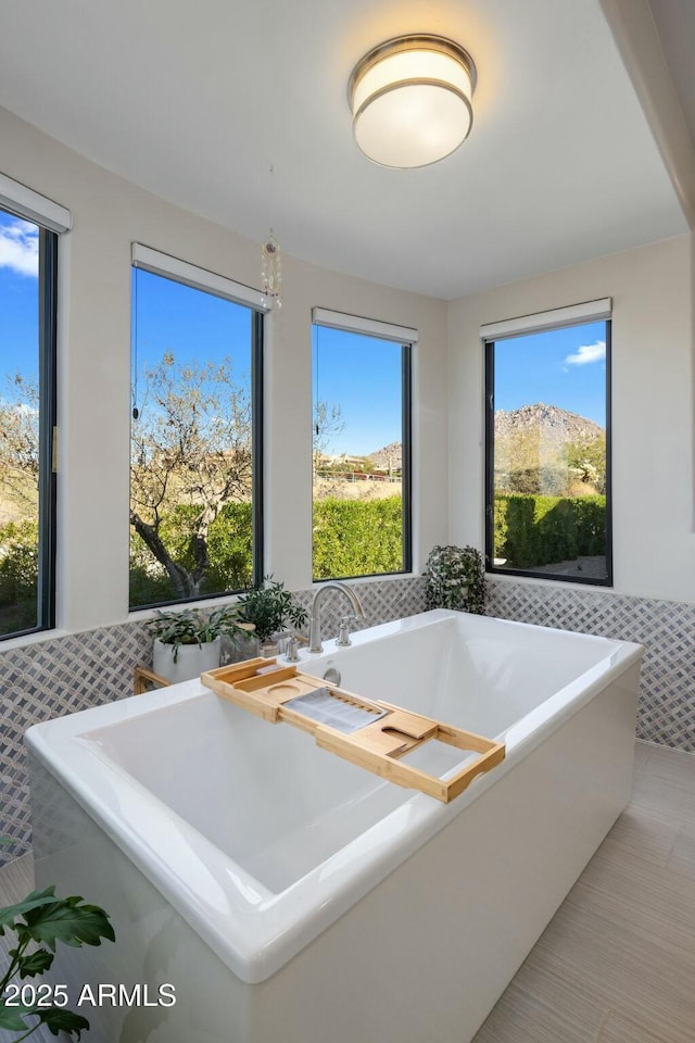 full bath with a freestanding bath, tile patterned flooring, a wainscoted wall, and tile walls