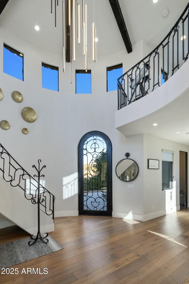 foyer with a towering ceiling, wood-type flooring, a healthy amount of sunlight, baseboards, and beam ceiling