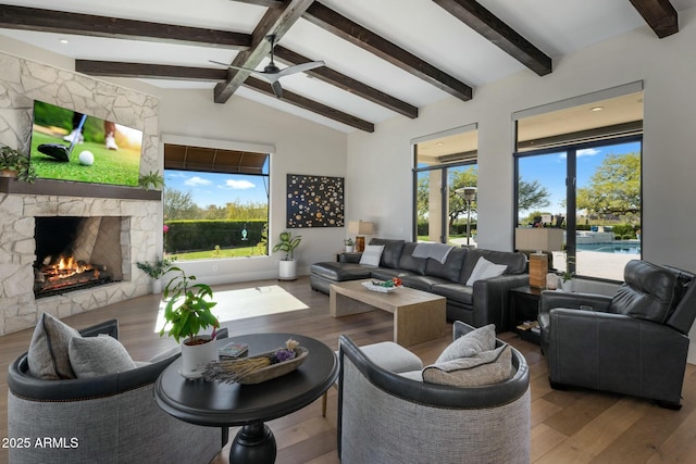 living area featuring a stone fireplace, vaulted ceiling with beams, ceiling fan, and wood finished floors