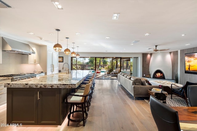 kitchen with wall chimney range hood, light stone counters, light hardwood / wood-style flooring, a spacious island, and pendant lighting