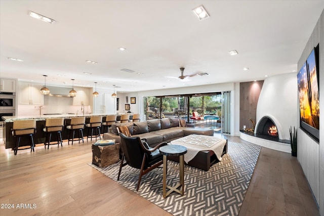 living room featuring a fireplace, ceiling fan, sink, and light wood-type flooring