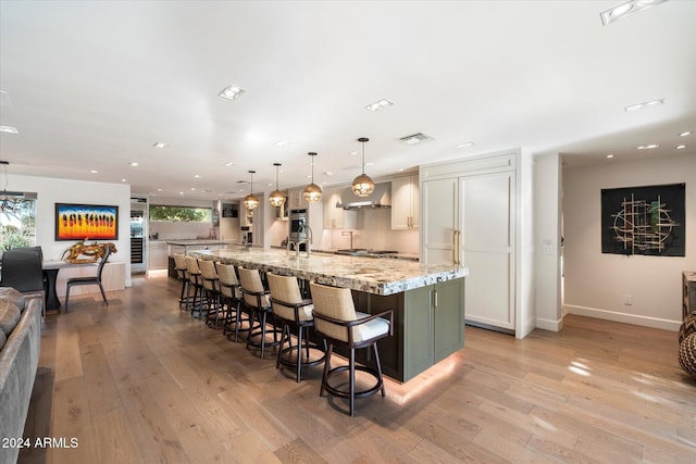 kitchen featuring a large island with sink, a kitchen breakfast bar, hanging light fixtures, light hardwood / wood-style flooring, and light stone countertops