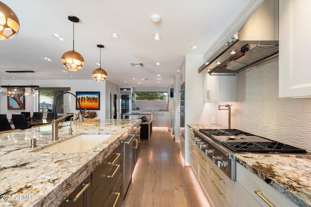 kitchen featuring sink, wall chimney range hood, pendant lighting, white cabinets, and stainless steel gas stovetop