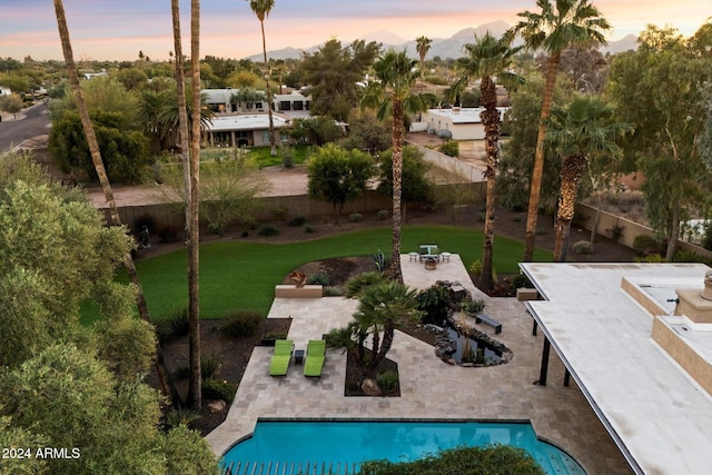 pool at dusk featuring a lawn and a patio area