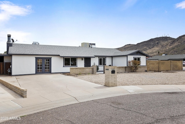 ranch-style home featuring a fenced front yard, french doors, brick siding, and a mountain view