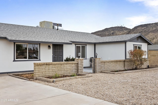 ranch-style house with brick siding, fence, a mountain view, and roof with shingles