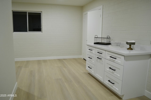 bar with light hardwood / wood-style floors, white cabinetry, and brick wall