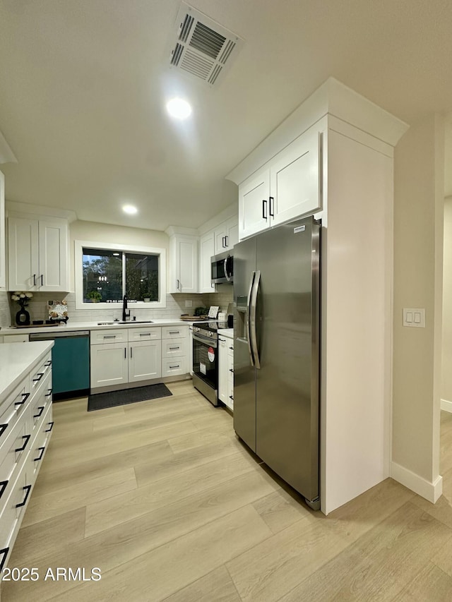 kitchen with light hardwood / wood-style flooring, appliances with stainless steel finishes, sink, backsplash, and white cabinets