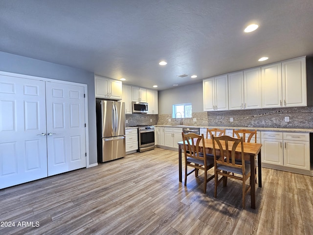 kitchen featuring white cabinets, stainless steel appliances, light countertops, light wood-style floors, and a sink