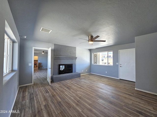 unfurnished living room with dark wood-style floors, a fireplace, visible vents, ceiling fan, and baseboards