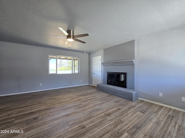 unfurnished living room featuring a textured ceiling, wood finished floors, a ceiling fan, baseboards, and a glass covered fireplace