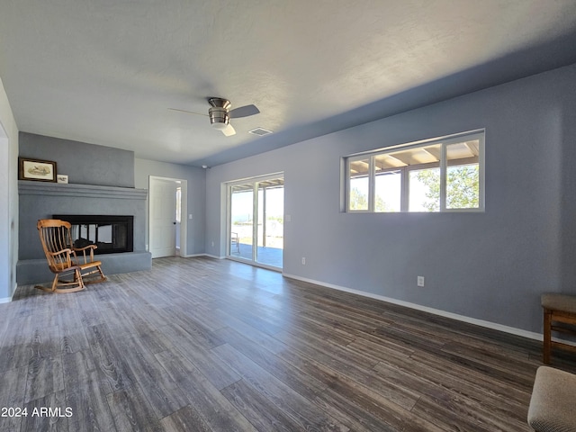 unfurnished living room with baseboards, visible vents, dark wood-type flooring, and a glass covered fireplace