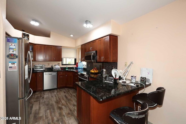 kitchen featuring a peninsula, dark wood-style flooring, vaulted ceiling, appliances with stainless steel finishes, and decorative backsplash