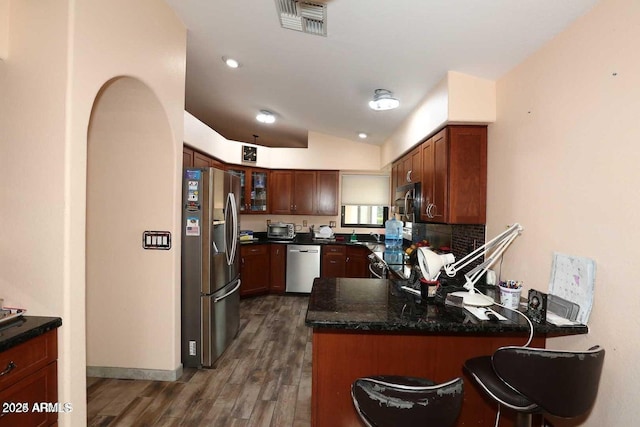 kitchen with lofted ceiling, stainless steel appliances, a peninsula, dark wood-style flooring, and visible vents