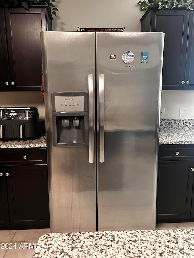 kitchen with light tile patterned flooring, light stone counters, and stainless steel fridge