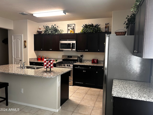 kitchen featuring light tile patterned flooring, stainless steel appliances, sink, a kitchen breakfast bar, and a kitchen island with sink