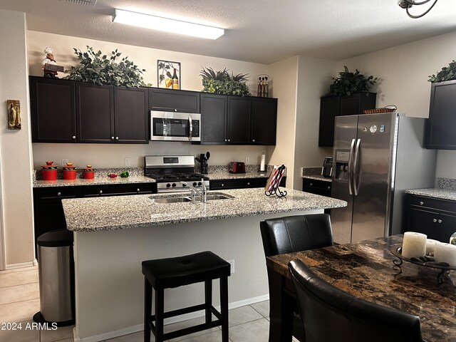 kitchen with a breakfast bar, appliances with stainless steel finishes, light tile patterned floors, and light stone countertops