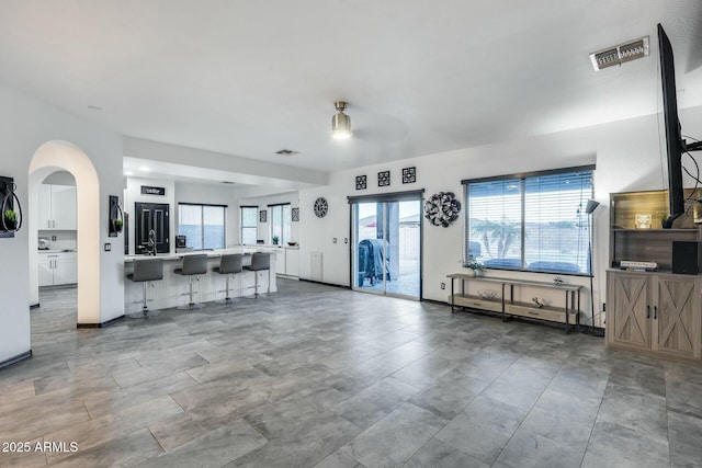 unfurnished living room featuring visible vents, a sink, baseboards, and arched walkways