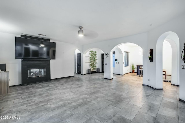 unfurnished living room with ceiling fan, arched walkways, a multi sided fireplace, baseboards, and visible vents