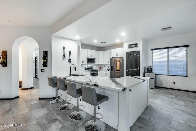 kitchen featuring visible vents, a peninsula, light stone counters, a sink, and appliances with stainless steel finishes