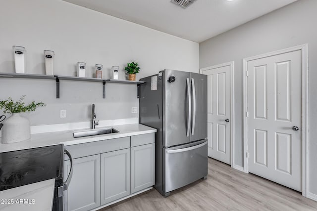 kitchen featuring open shelves, freestanding refrigerator, electric range, light countertops, and a sink