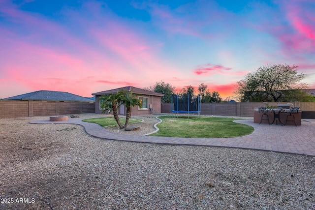 yard at dusk featuring a fenced backyard, a trampoline, and a patio area
