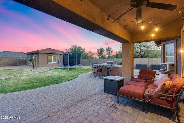 patio terrace at dusk featuring a yard, a fenced backyard, and a trampoline