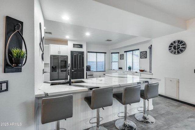 kitchen featuring visible vents, stainless steel fridge with ice dispenser, a peninsula, a breakfast bar, and white cabinetry