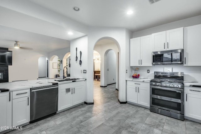 kitchen featuring appliances with stainless steel finishes, a sink, arched walkways, white cabinetry, and recessed lighting