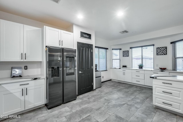 kitchen with white cabinets, stainless steel refrigerator with ice dispenser, and visible vents