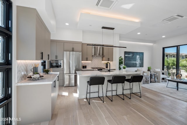 kitchen featuring gray cabinetry, appliances with stainless steel finishes, decorative light fixtures, a large island with sink, and light hardwood / wood-style floors