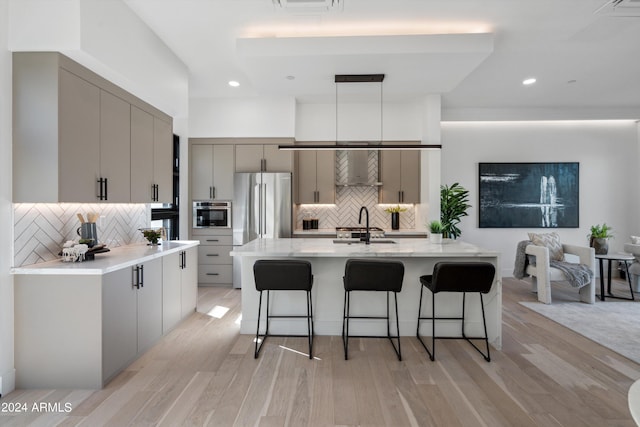 kitchen with gray cabinetry, decorative light fixtures, light hardwood / wood-style floors, a breakfast bar area, and a kitchen island with sink