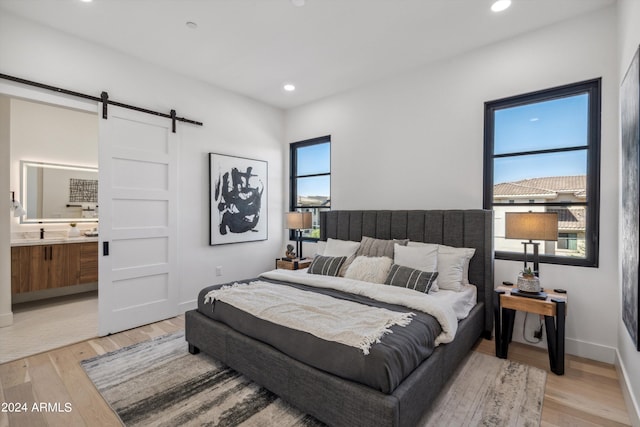 bedroom with a barn door, ensuite bathroom, and light hardwood / wood-style flooring