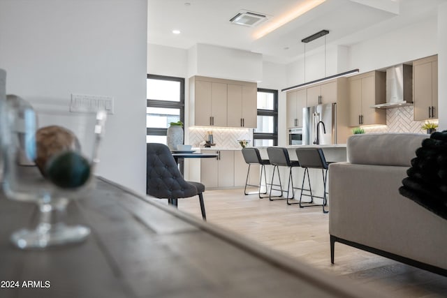 kitchen with light wood-type flooring, appliances with stainless steel finishes, tasteful backsplash, and wall chimney range hood