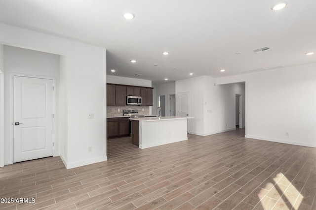 kitchen with a kitchen island with sink, dark brown cabinets, and light hardwood / wood-style flooring