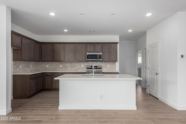 kitchen featuring tasteful backsplash, stainless steel appliances, a kitchen island with sink, and dark brown cabinets