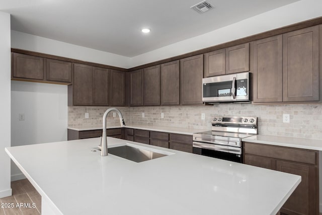 kitchen featuring appliances with stainless steel finishes, an island with sink, sink, backsplash, and dark brown cabinets