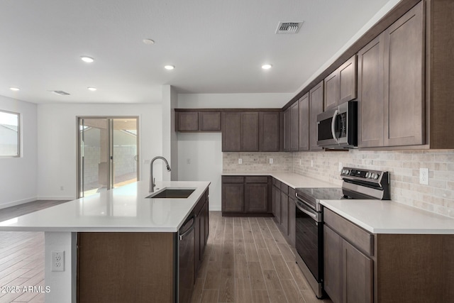 kitchen with appliances with stainless steel finishes, tasteful backsplash, sink, a kitchen island with sink, and light hardwood / wood-style floors