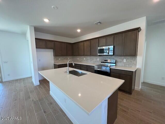 kitchen with sink, backsplash, a center island with sink, and appliances with stainless steel finishes