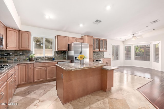 kitchen featuring sink, tasteful backsplash, light stone counters, a kitchen island, and stainless steel appliances