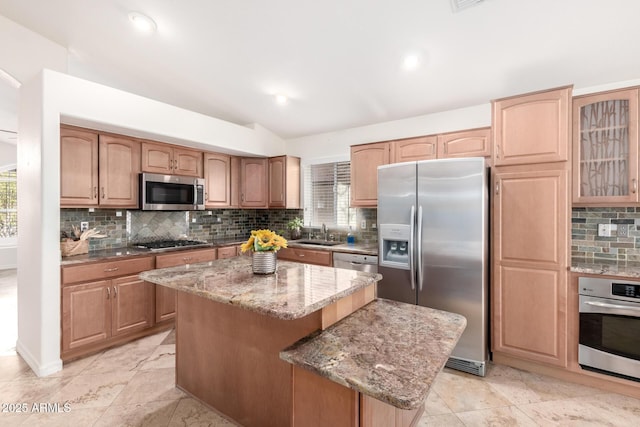 kitchen with appliances with stainless steel finishes, tasteful backsplash, sink, a center island, and light stone countertops