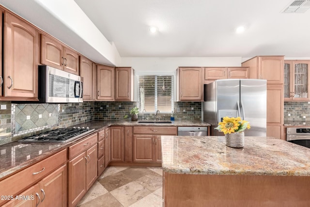 kitchen with tasteful backsplash, appliances with stainless steel finishes, sink, and light stone counters