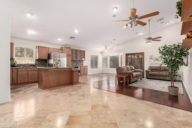 kitchen featuring a kitchen island, high vaulted ceiling, stainless steel refrigerator, sink, and backsplash