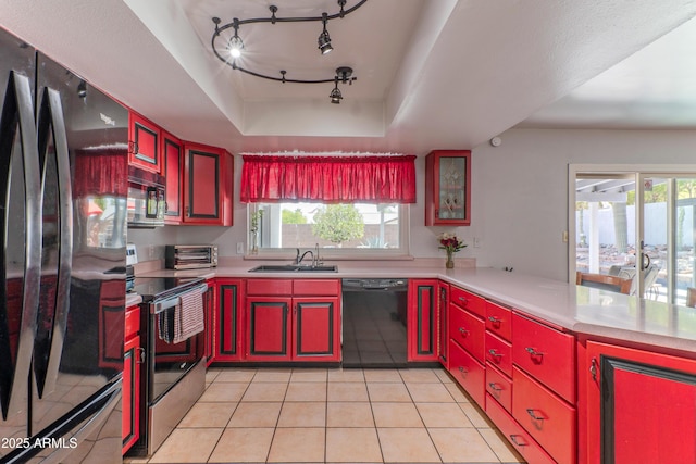 kitchen featuring black appliances, a tray ceiling, red cabinetry, and a sink