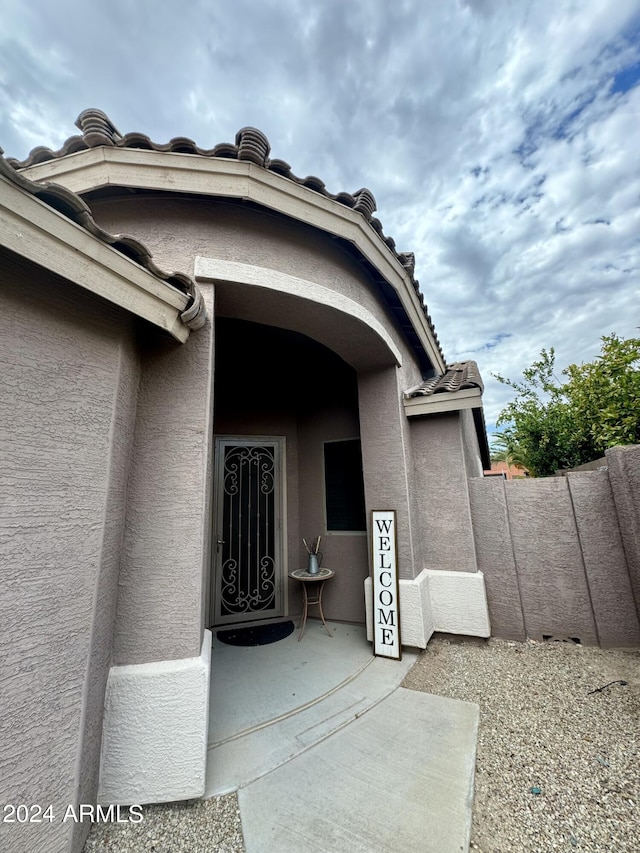 view of exterior entry featuring a tile roof, fence, and stucco siding