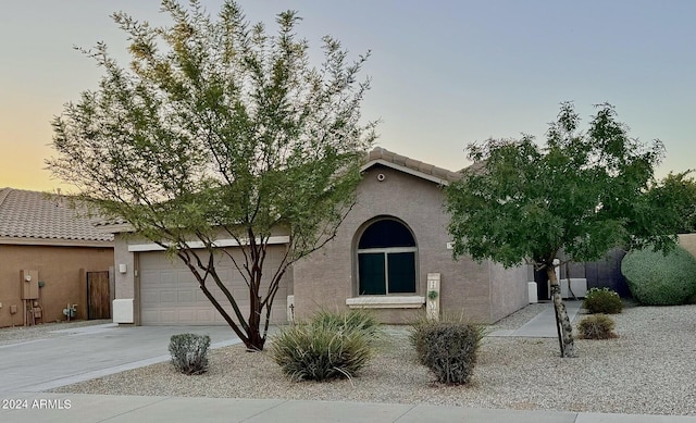 view of property hidden behind natural elements featuring a garage, a tile roof, driveway, and stucco siding