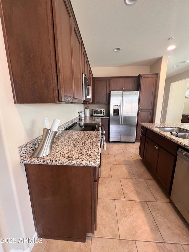 kitchen featuring sink, light stone counters, light tile patterned flooring, dark brown cabinets, and appliances with stainless steel finishes